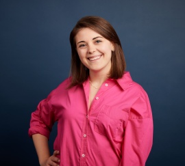 Sarah Grucza wears a pink shirt standing against a blue background