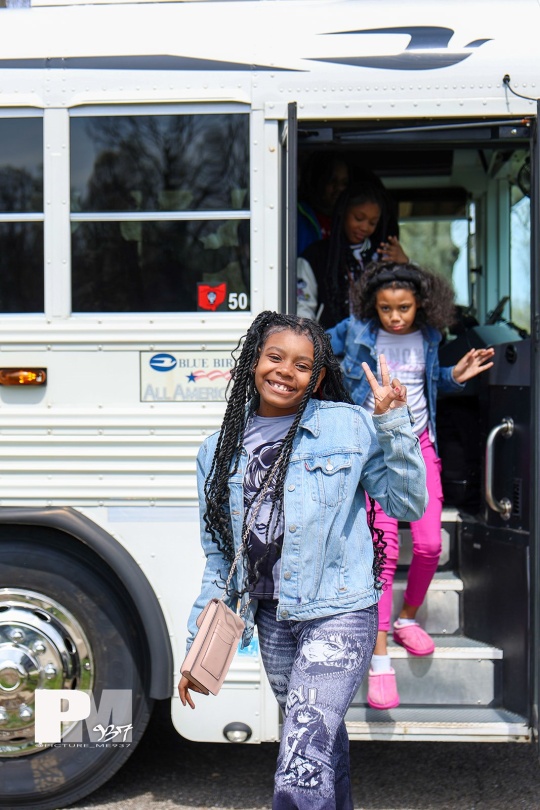 A child holds up a peace sign as she walks off a school bus
